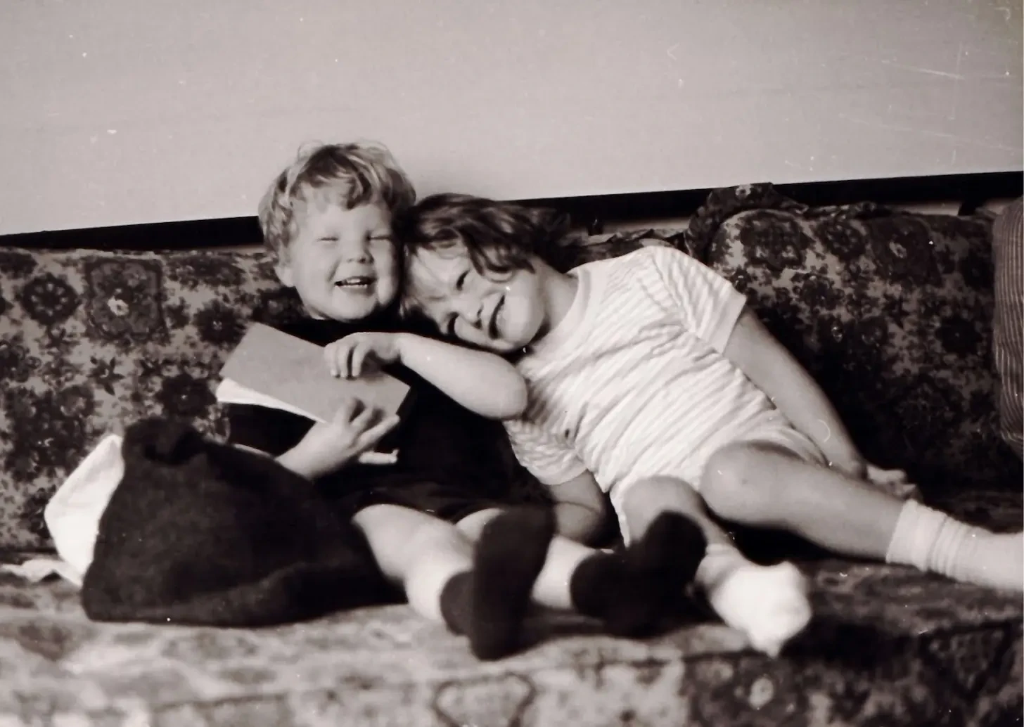 Young Anne and her brother Jeff laughing together on a sofa